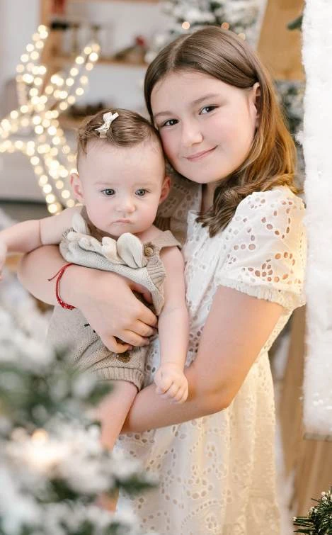 Duas crianças abraçadas ao lado da árvore de Natal