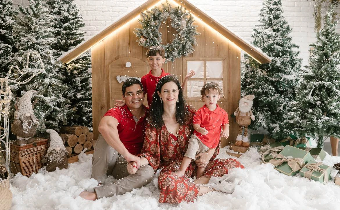 Família reunida diante da casinha de Natal, com roupas em tons vermelhos