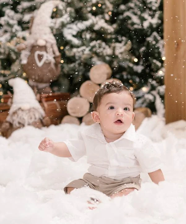 Bebê sentado em um cenário com árvore de Natal e ursinho